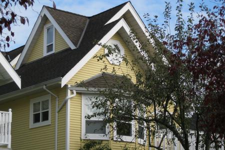 A yellow craftsman heritage house with white trim and a brown roof